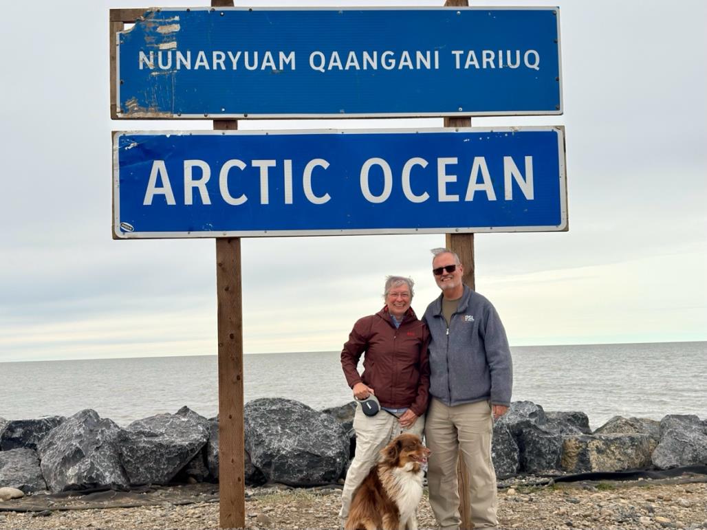 Amy, her husband, and their dog standing beside the Arctic Ocean road sign