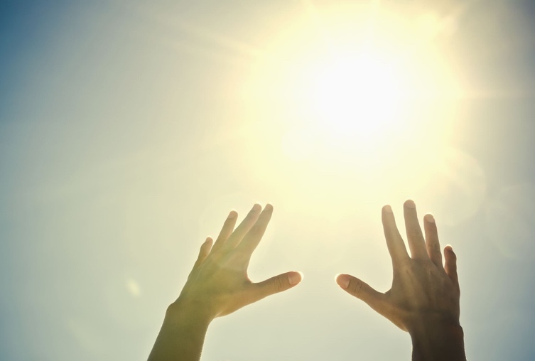 Two hands reaching up toward bright sunlight