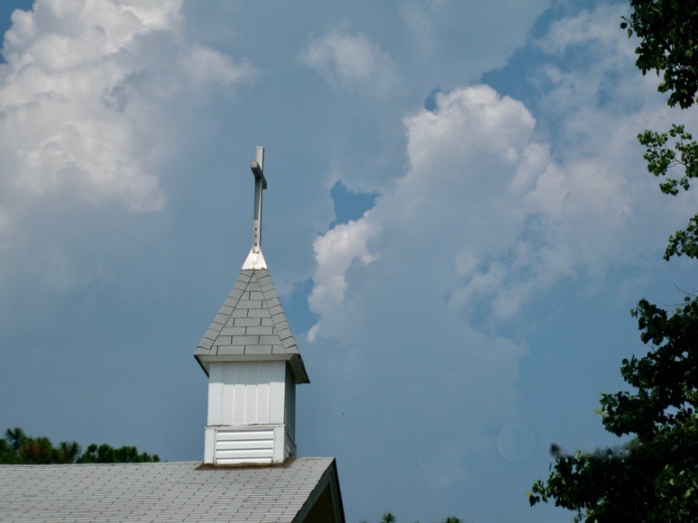 A white church steeple with a cross against a cloudy sky