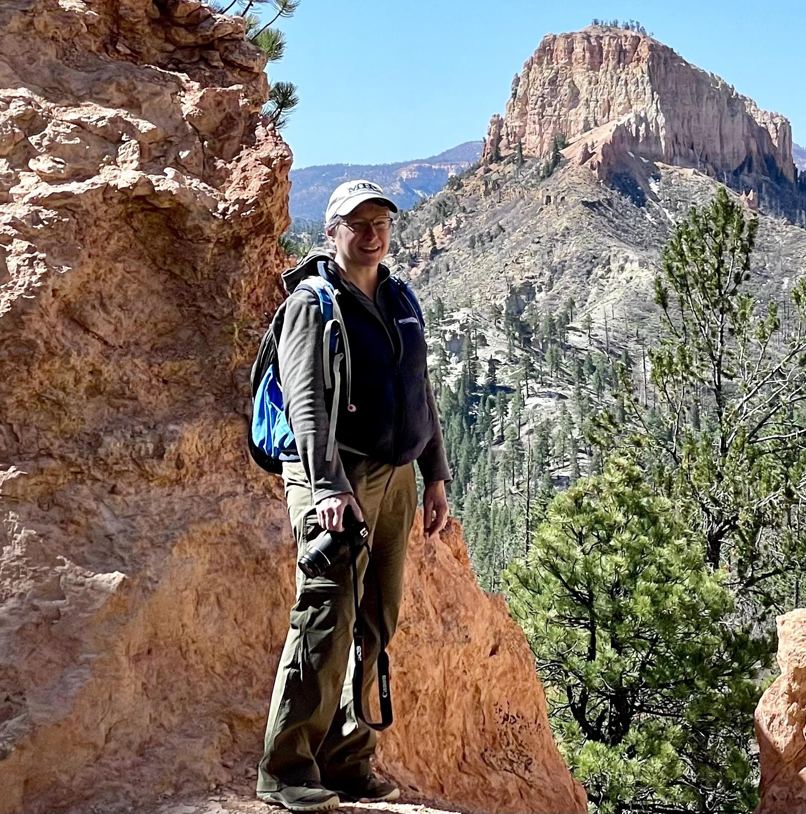 Amy standing on a rocky ledge with red rock canyon formations behind her